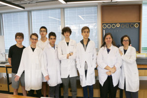 Grupo de alunos com jaleco branco e coma professora doutora bióloga Luciana Vasques na sala STEAM do Colégio Miguel de Cervantes
